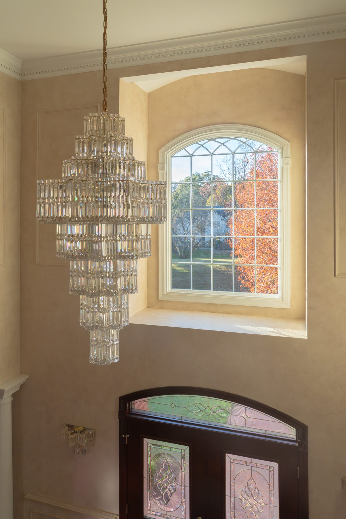 Tall white Vytex Fortis arched specialty window with sunburst grille in a two-story foyer
